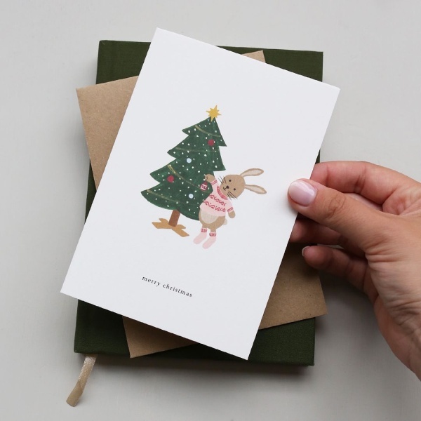 Postal de Kartotek con árbol de Navidad y conejo con el texto "Feliz Navidad".